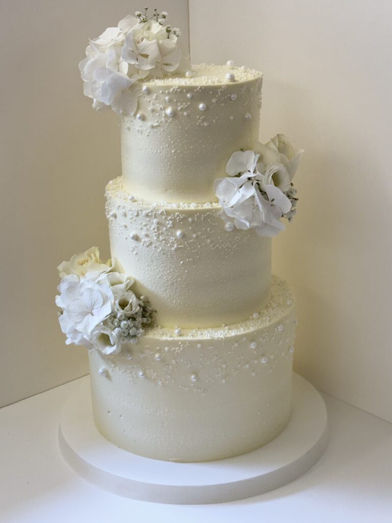 Dreistöckige weiße Hochzeitstorte mit weißen Blüten