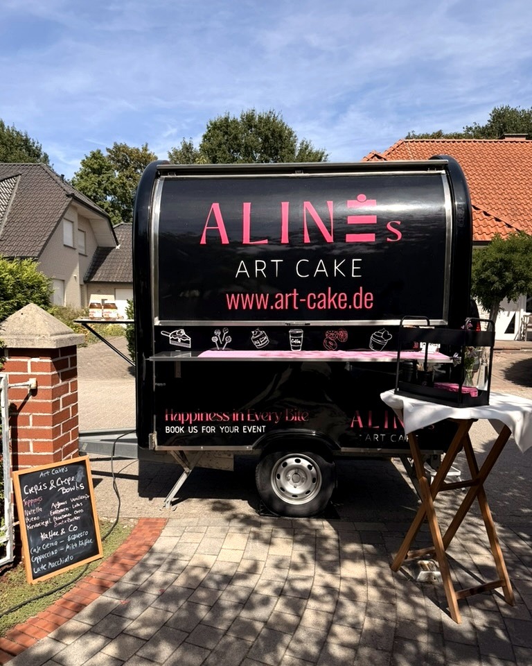 Der kleine Wagen von Art Cake: schwarzer Anhänger mit pinkem Logo, davor eine Tafel mit dem Angebot.