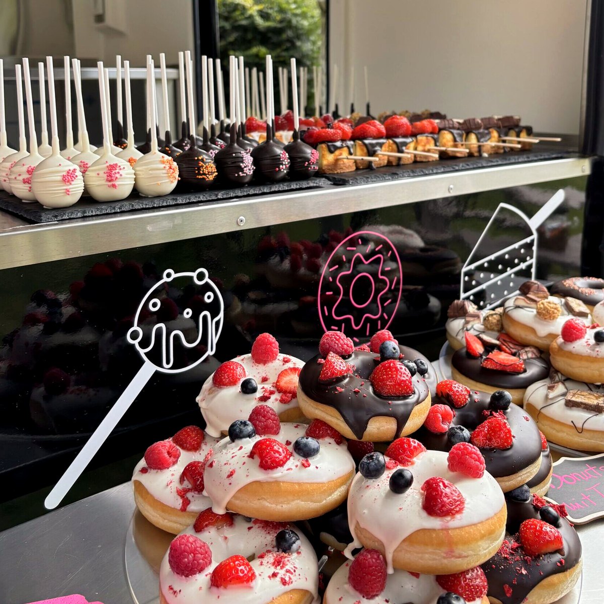 Auslage des Wagens mit Cake Pops, Cheesecake am Stiel und Donuts mit Beeren.
